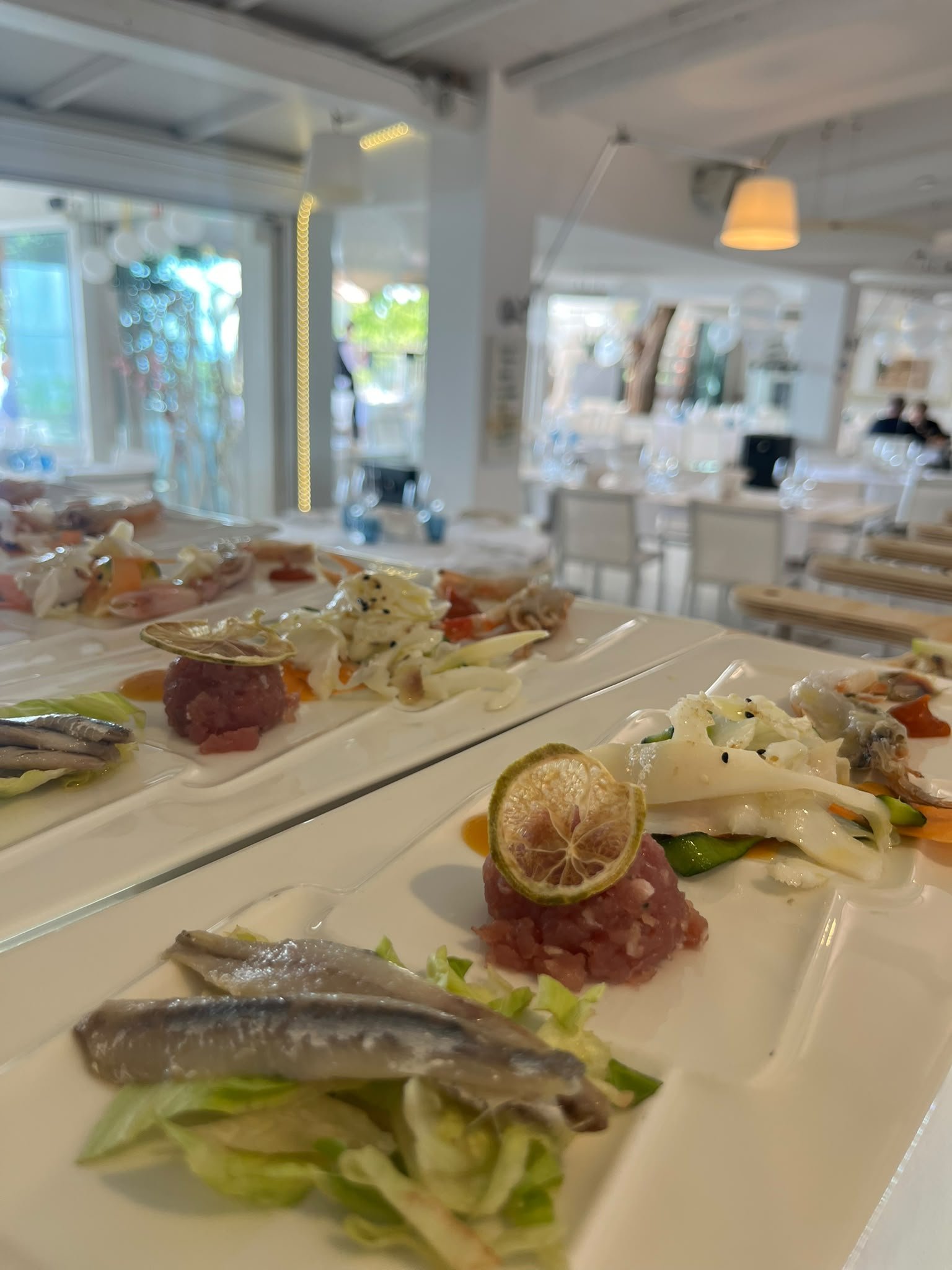 Piatti rettangolari bianchi con alici marinate, tartare di tonno e lime essiccato in una sala luminosa del Ristorante della Rosa